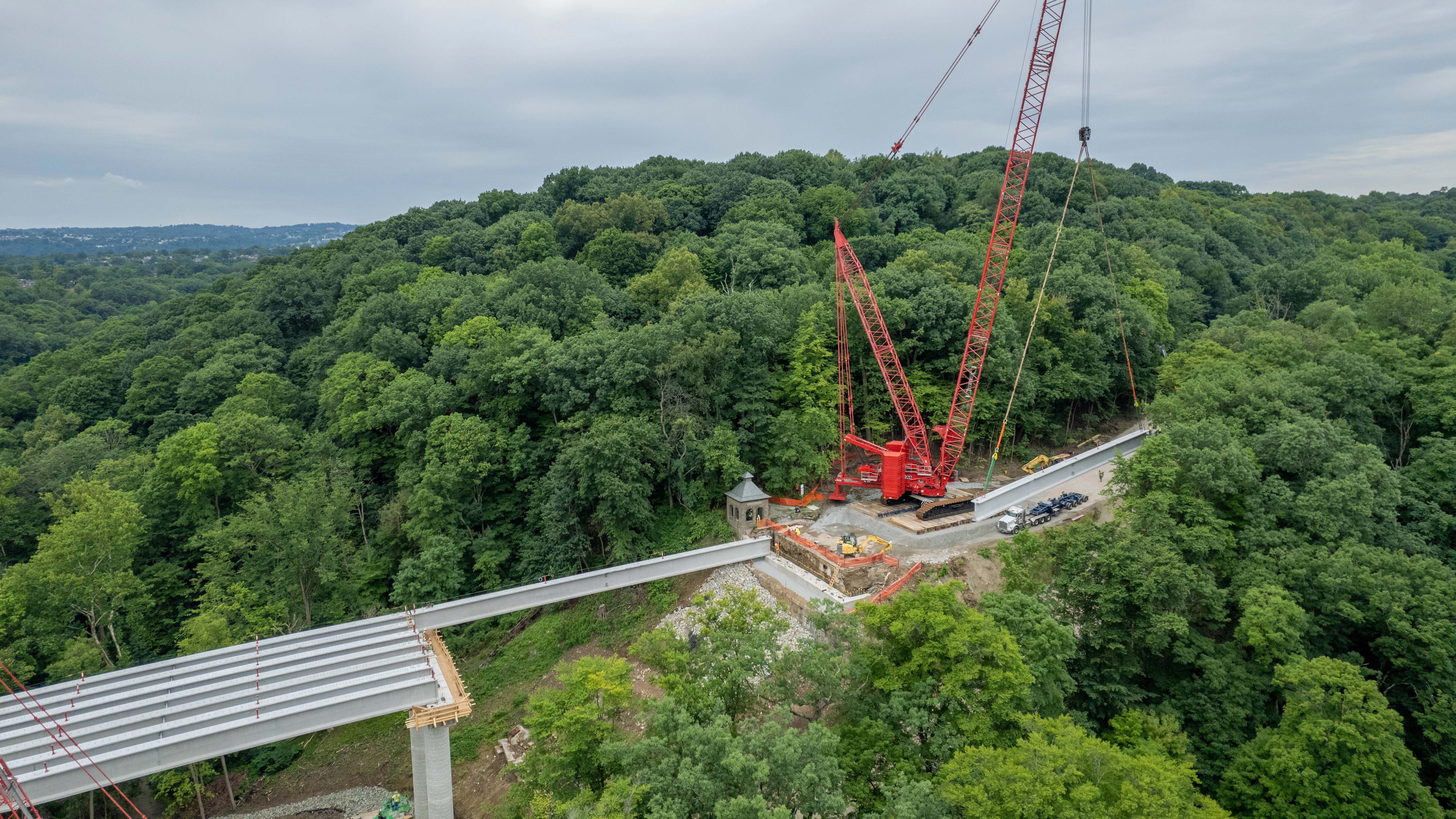 An image of a large red crane lifting and placing bridge beams during the rebuilding of the Fern Hollow Bridge 